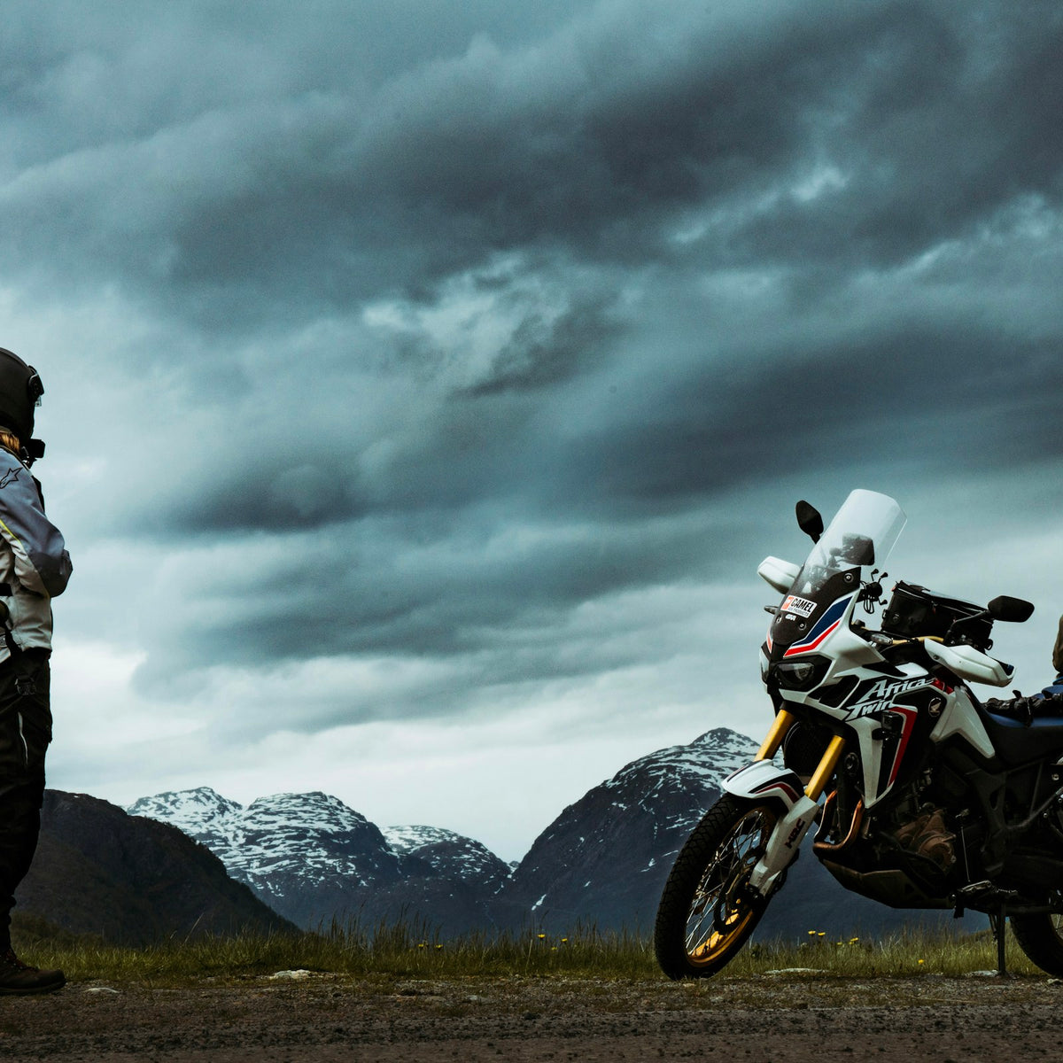 Rider in an adventure touring suit beside a motorcycle in the mountains